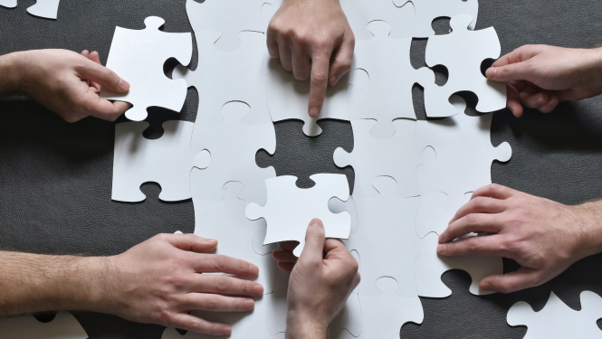 vairākas rokas uz galda liek kopa puzles gabaliņus