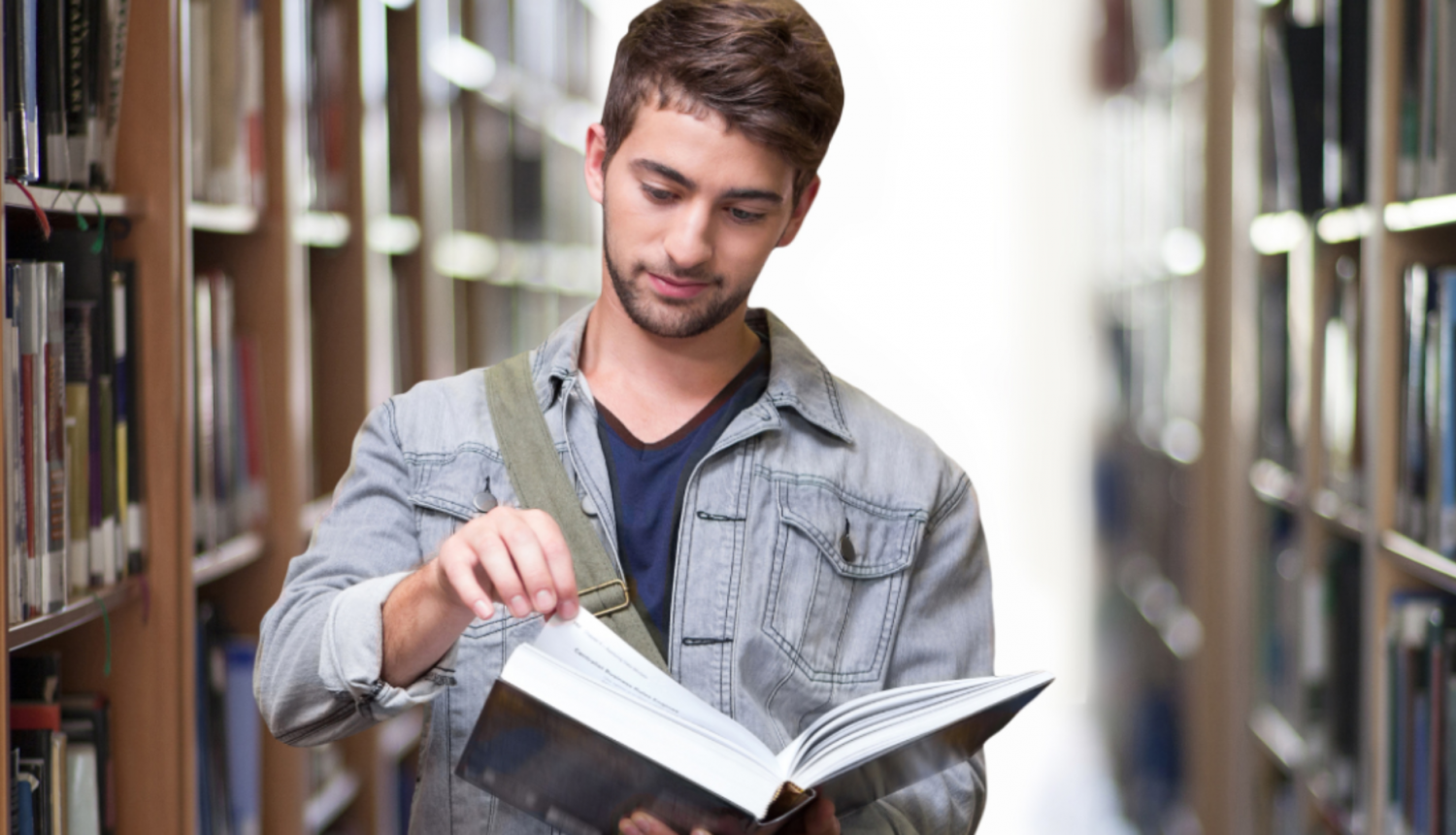 Vīrietis lasa grāmatu bibliotēkā